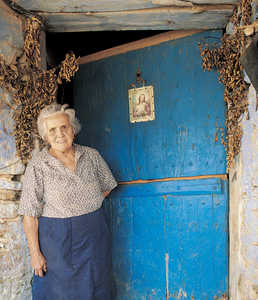 98.	Maria Manterola espera ante la puerta del caserio Aranburu Zahar (Aia), protegida por los ramos de San Juan y por una estampa moderna del Sagrado Corazon de Jesus.